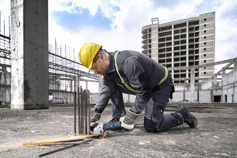 A person wearing safety equipment cuts rebar with a power tool at a construction site.