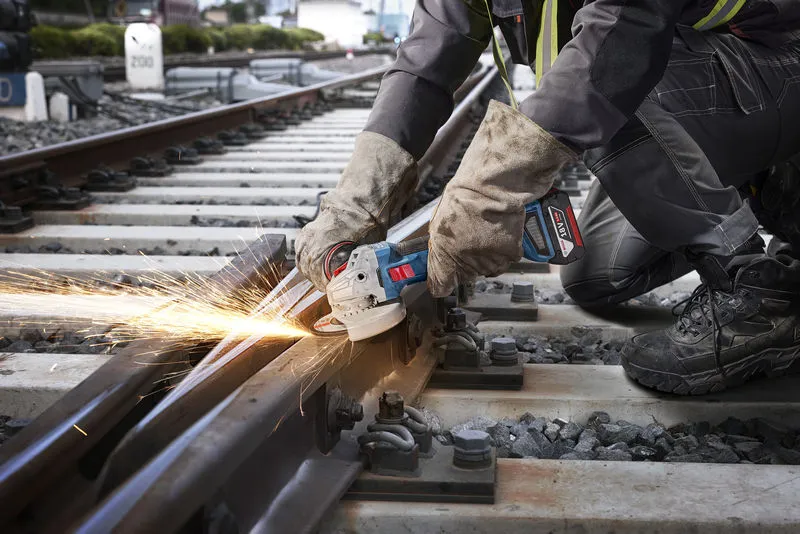 GWS 18V-11 S A person wearing safety equipment cuts a railway track with a cordless angle grinder.