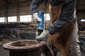 A person wearing safety equipment uses a straight grinder to grind metal, creating sparks.