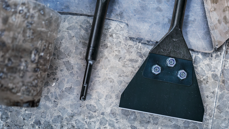 Floor scraper attachment lying on a stone surface beside a worn mallet.