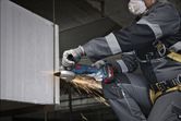 A person wearing safety equipment grinds a metal beam, creating sparks.