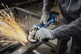 A person wearing safety equipment grinds a metal frame with an angle grinder.