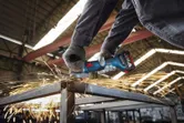 A person wearing safety equipment grinds a metal beam, producing bright sparks.