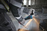 A person wearing safety equipment cuts metal, using an angle grinder with sparks flying.