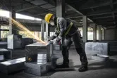 A person wearing safety equipment grinds metal ductwork, producing sparks.