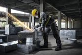 A person wearing safety equipment grinds metal ductwork, producing sparks.