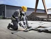 A person wearing safety equipment uses an angle grinder to cut metal outdoors.