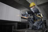 A person wearing safety equipment grinds metal on a construction site.