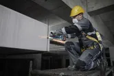 A person wearing safety equipment grinds metal on a construction site.
