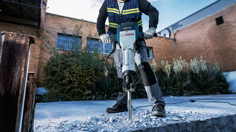 PRO HEX-4C Flat Chisel 28 mm, 35 x 400 mm A person wearing safety equipment breaks concrete with a demolition hammer outdoors.