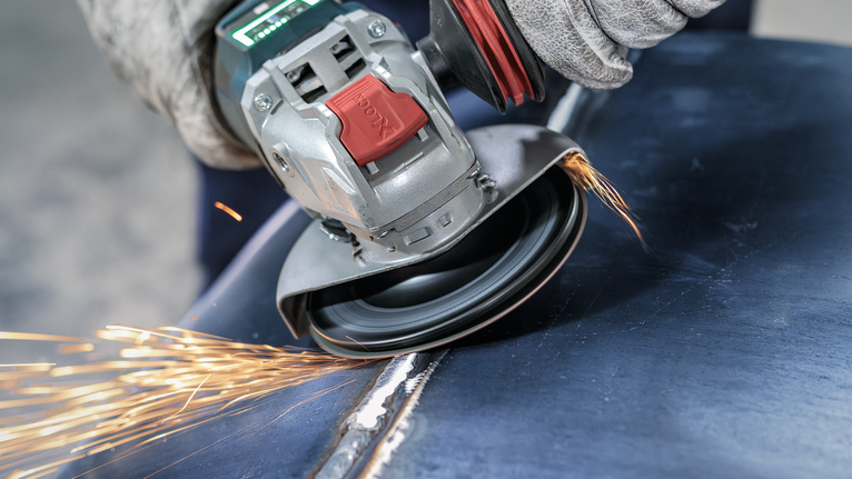 PRO Backing Pad Hard, 125 mm, X-Lock Person wearing safety equipment uses an angle grinder to smooth a metal weld.