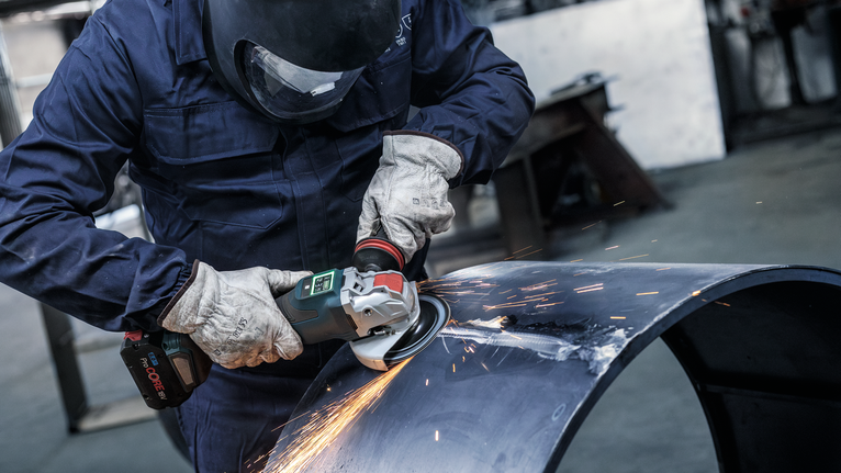 PRO Backing Pad Clip, X-Lock A person wearing safety equipment grinds metal pipe, creating bright sparks.