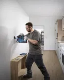 A person wearing safety equipment drills into a wall inside a kitchen.
