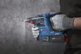 A person wearing safety equipment drills into a concrete wall with a rotary hammer.
