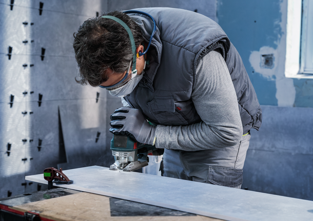 PRO Soft Tile T130RF Jigsaw Blade, 83 mm, 3 pcs Person wearing safety equipment uses a jigsaw to cut a board.