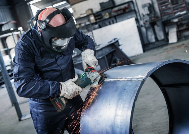 PRO Backing Pad Hard, 125 mm, X-Lock Person wearing safety equipment grinds a large metal pipe, creating sparks.
