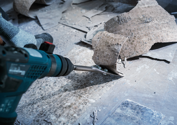 Person wearing safety equipment uses a power tool to remove old flooring material.