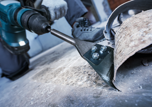 A person wearing safety equipment uses a power tool to remove flooring.