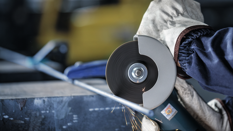 Person wearing safety equipment cuts metal pipe using an angle grinder.
