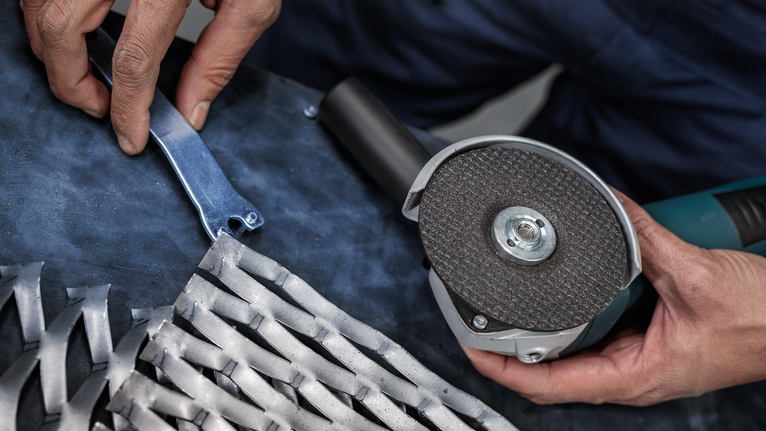 PRO Semi-Flexible Grinding Disc, 100 x 2 x 16 mm Person holding an angle grinder and a tool key next to a metal grid.