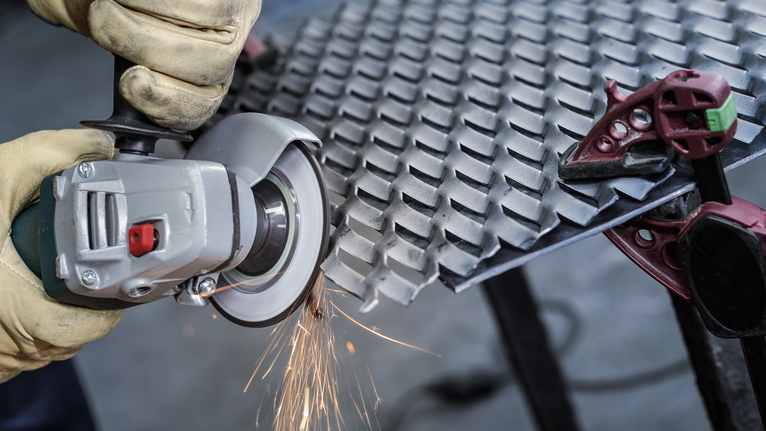 PRO Semi-Flexible Grinding Disc, 100 x 2 x 16 mm Person wearing safety equipment uses an angle grinder to cut a metal sheet.