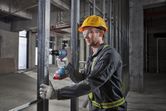 A person wearing safety equipment uses a cordless drill on a metal frame.