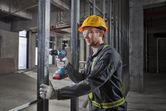 A person wearing safety equipment drills into metal framing at a construction site.