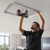 A person wearing safety equipment uses a power drill to install a ceiling light fixture.