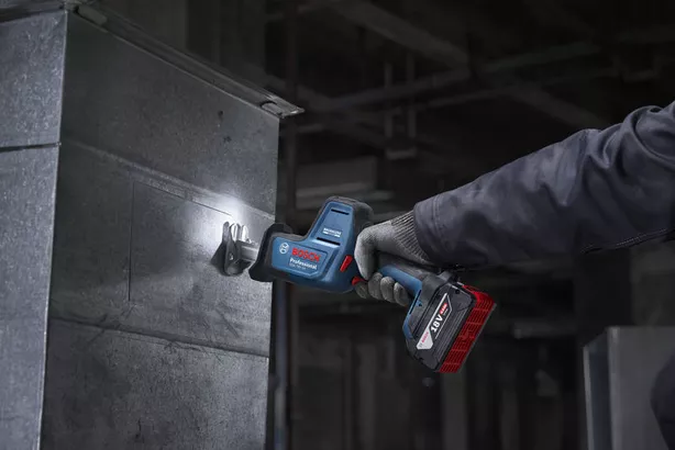 A person wearing safety equipment cuts sheet metal with a cordless reciprocating saw.