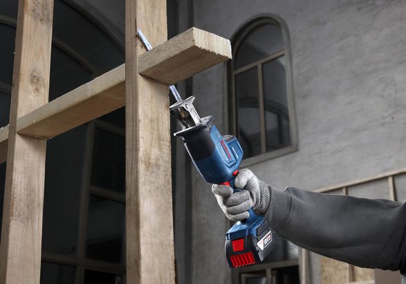A person wearing safety equipment uses a reciprocating saw to cut wooden beams.