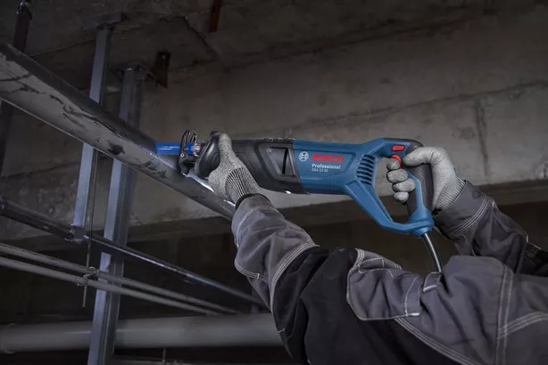 A person wearing safety equipment cuts a metal pipe with a reciprocating saw.