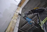 A person wearing safety equipment uses a reciprocating saw to cut into a wall.