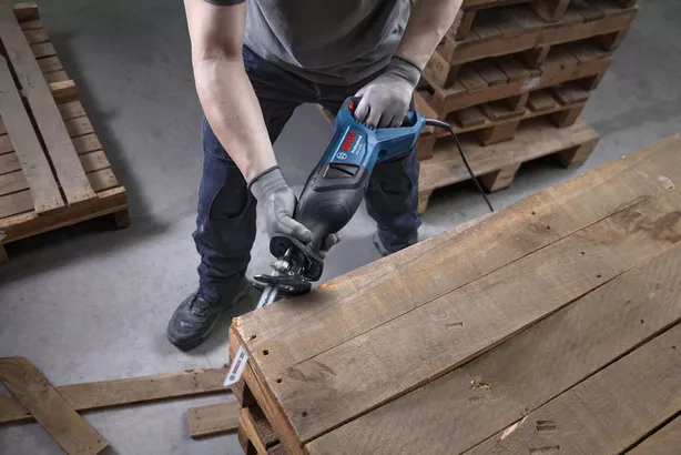 A person wearing safety equipment uses a reciprocating saw to cut a wooden pallet.