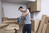 A person wearing safety equipment drills into wood using a cordless rotary hammer.