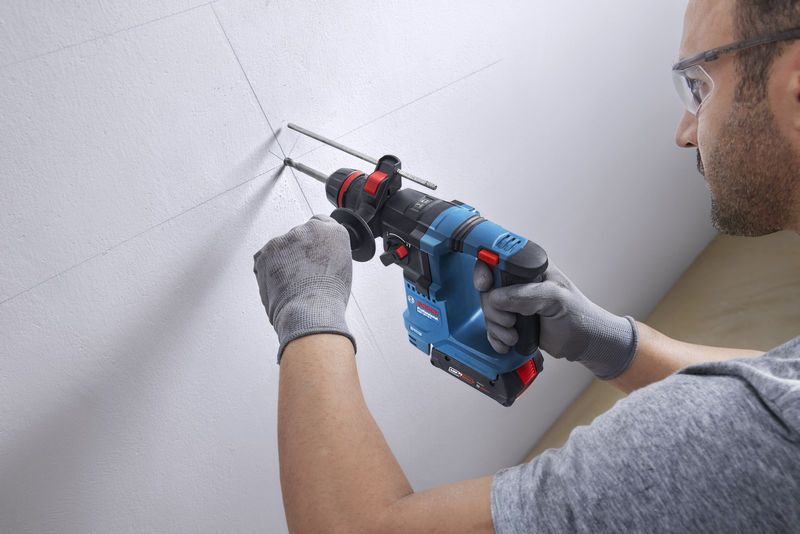 GBH 18V-18 X A person wearing safety equipment drills a hole into a marked wall with a cordless rotary hammer.