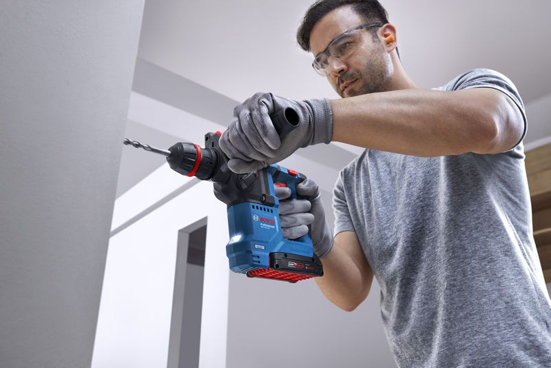 GBH 18V-18 X A person wearing safety equipment drills into a concrete wall using a cordless rotary hammer.