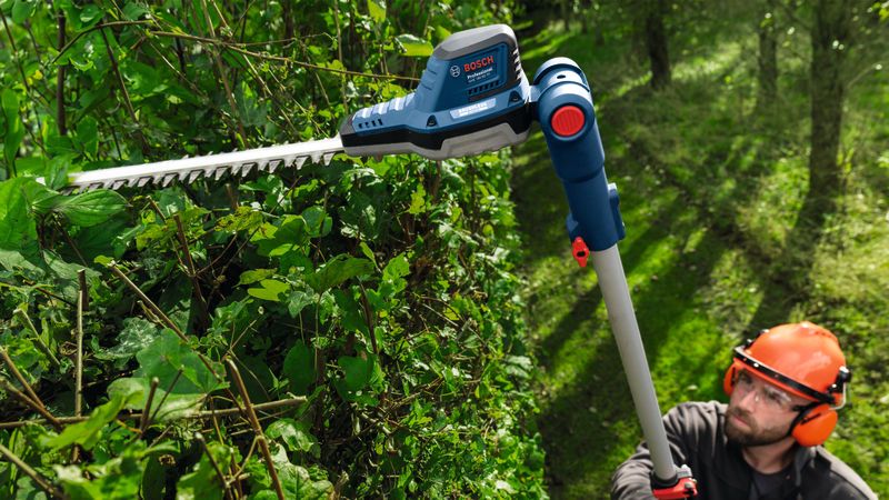 GHE 18V-50 TP A person wearing safety equipment trims tall hedges using a cordless telescopic hedgecutter.
