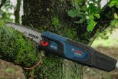 Chainsaw cutting through a tree branch outdoors in a forested area.