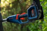 Person wearing safety equipment holds a cordless power tool outdoors.