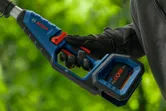 A person wearing safety equipment operates a cordless power tool outdoors.