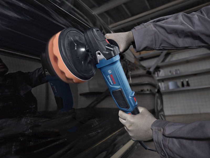 A person wearing safety equipment polishes a car door with a power polisher.