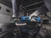 A person wearing safety equipment polishes a car hood with a blue polisher.