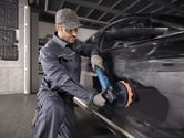 A person wearing safety equipment polishes a black car using a power tool.