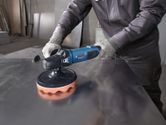 A person wearing safety equipment polishes a metal surface with a power tool.