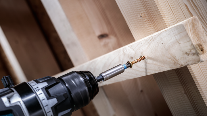 Cordless drill driving a screw into a wooden beam.