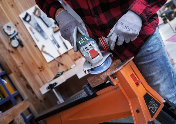Object #200557592: 7425288_APP_WIDE_5 Person wearing safety equipment uses an angle grinder to sand wood clamped to a workbench.