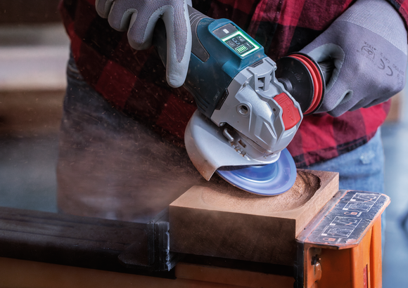 Object #200557595: 7425288_APP_WIDE_3 Worker wearing safety equipment uses an angle grinder to carve a circular hole in wood.