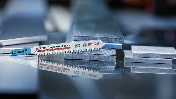 Object #200559112: 7478951_app_web_2 Jigsaw blade resting on stacked metal sheets in a workshop setting.