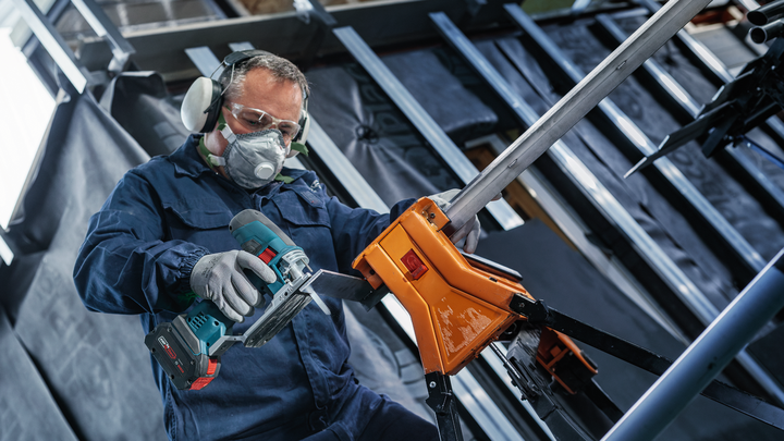 Object #200559114: 7478951_app_web_4 Person wearing safety equipment drills into a metal beam held by an orange vise.