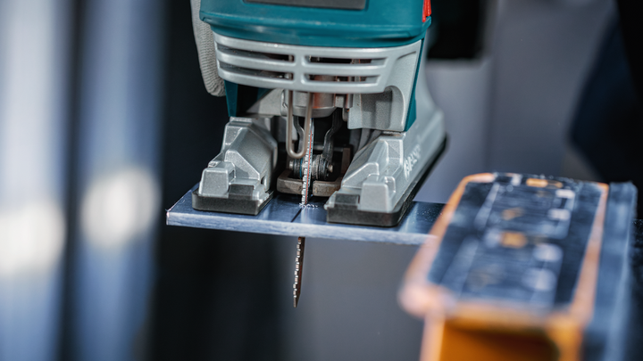Object #200559117: 7478951_app_web_7 Jigsaw cutting through a sheet of metal on a workbench.